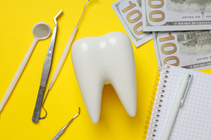 The Struggle with Insurance Companies: Can Dentists Find Balance? Dental tools, money, decorative tooth and notepad on yellow background, closeup